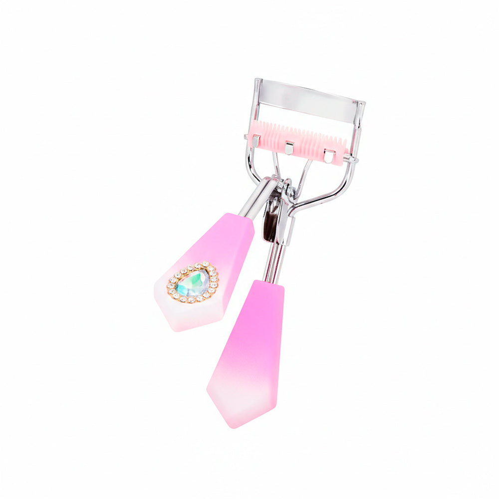 Rizador de pestañas Strass Heart Curl con mango facetado fucsia degradé, detalle corazón strass turquesa y cerdas integradas rosa sobre fondo blanco
