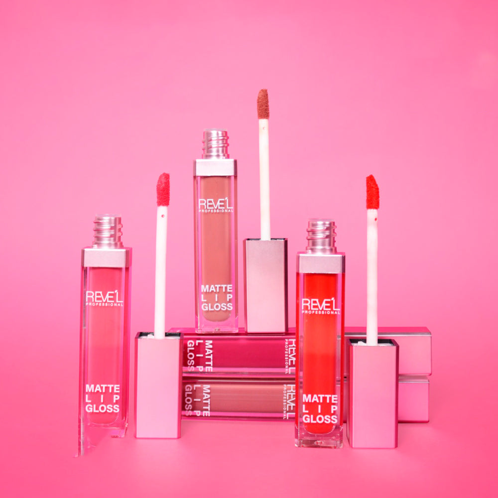 Lip gloss matte Reve'l Professional con empaque rosa y tapa plateada, aplicador suave, tonos nude, fucsia y rojo vibrante, sobre fondo rosa