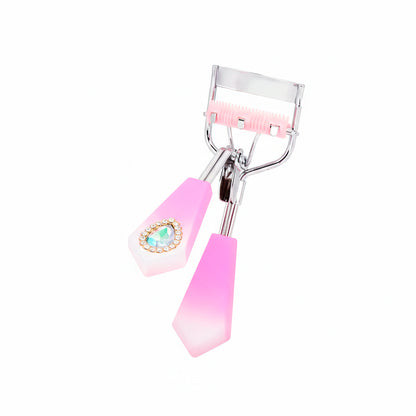Rizador de pestañas Strass Heart Curl con mango facetado fucsia degradé, detalle corazón strass turquesa y cerdas integradas rosa sobre fondo blanco