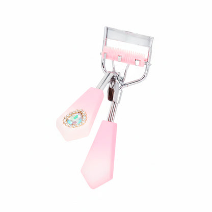 Rizador de pestañas Strass Heart Curl con mango facetado rosa palo degradé, detalle corazón strass y cerdas integradas rosa sobre fondo blanco