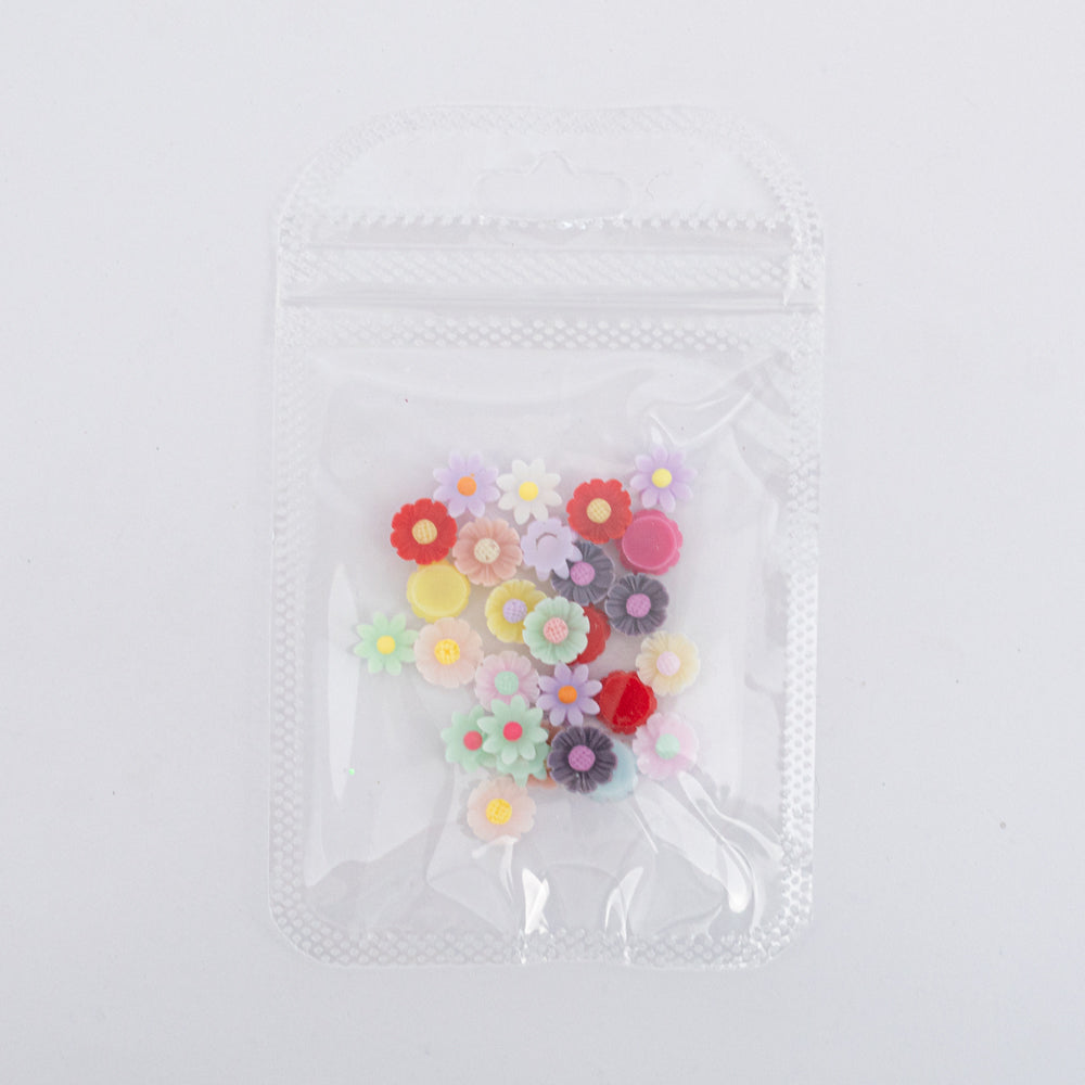 Dijes para uñas Nail Art de flores multicolor en resina en bolsa transparente sobre fondo blanco
