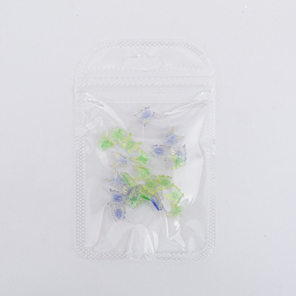 Dijes para uñas Nail Art de mariposas verde y azul con detalles dorados en bolsa transparente sobre fondo blanco