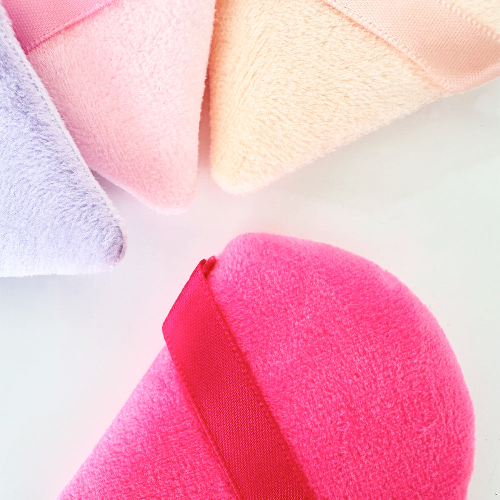 Detalle de textura de esponjas Powder Puff de terciopelo en colores lila, rosa, beige y fucsia con aro de dedo