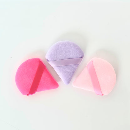 Set de esponjas Powder Puff de terciopelo en formas triangular, diamante y media luna en colores fucsia, lila y rosa con aro de dedo sobre fondo blanco