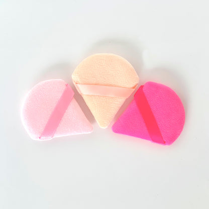 Set de esponjas Powder Puff de terciopelo en formas triangular, diamante y media luna en colores rosa, beige y fucsia con aro de dedo sobre fondo blanco
