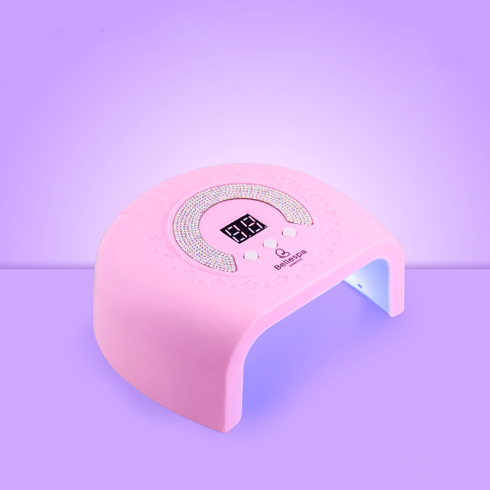 Lámpara UV LED para uñas Bellespa Cosmetics con pedrería en arco, pantalla digital y botones de control, color rosa suave sobre fondo lila