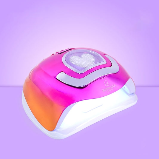 Lámpara UV LED para uñas Bellespa Cosmetics con acabado cromado, panel LED en forma de corazón con ribete plateado ondulado y base blanca, sobre fondo lila degradado