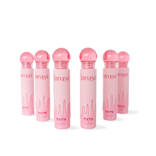 Lip gloss Jarusa Baby Lips con tapa bola rosa y empaque rosa pastel efecto drip, fórmula brillante e hidratante, sobre fondo blanco