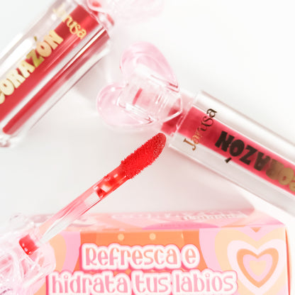 Close-up lifestyle shot with applicator and box Detalle de aplicador velvety Lip Gloss Corazón Hidratante Jarusa en tono rojo con caja que dice refresca e hidrata tus labios al fondo