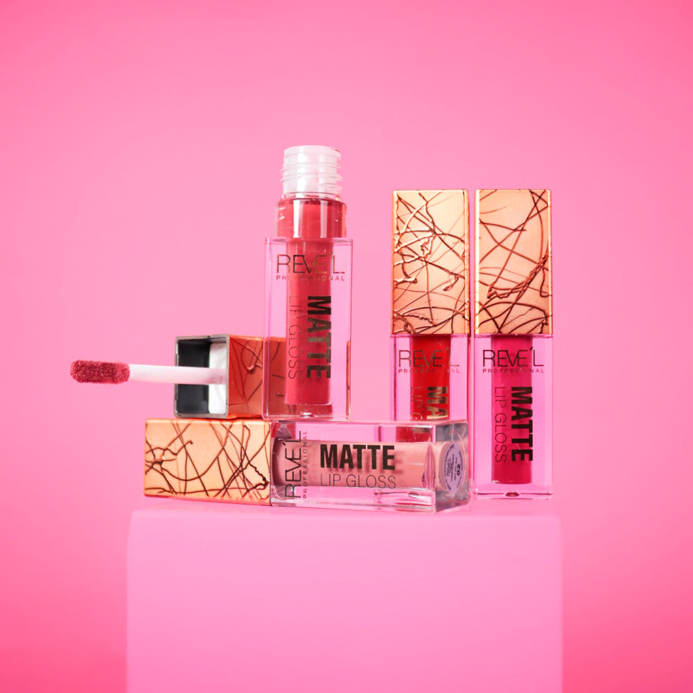 Lip gloss matte Reve'l Professional con tapa dorada texturizada y aplicador aterciopelado, tonos desde nude y rosa hasta rojo vibrante, sobre fondo rosa