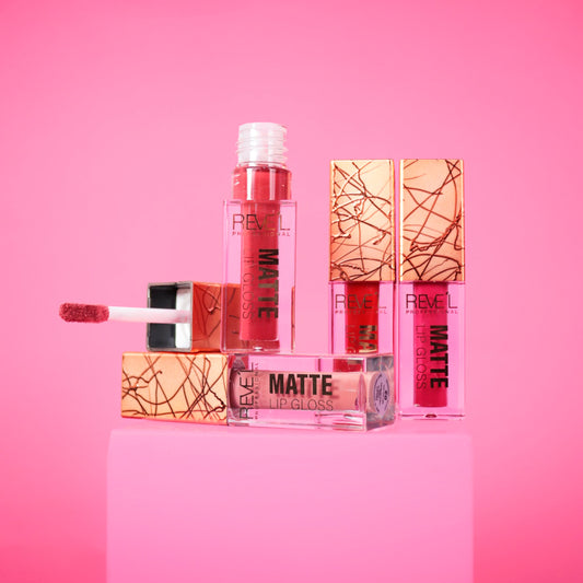 Lip gloss matte Reve'l Professional con tapa dorada texturizada y aplicador aterciopelado, tonos desde nude y rosa hasta rojo vibrante, sobre fondo rosa