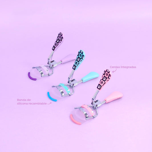 Rizador de pestañas con cerdas y silicona Skye Charm en colores lila, turquesa y rosa con estampado de huellas sobre fondo rosa pastel