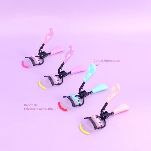 Rizador de pestañas Black Skye Charm con spoolie integrado y banda de silicona recambiable, en colores rosa, menta y durazno con diseño de huellas.