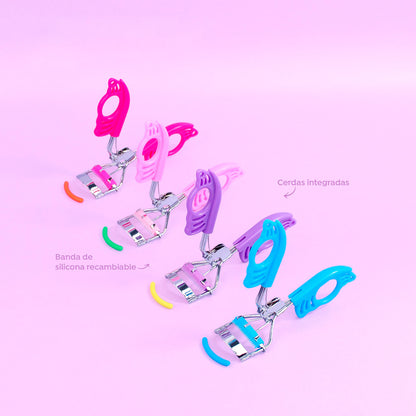 Rizador de pestañas Mariposa Curl Bellespa con mango calado diseño mariposa en colores fucsia, rosa, morado y celeste, cerdas integradas y banda de silicona recambiable sobre fondo rosa