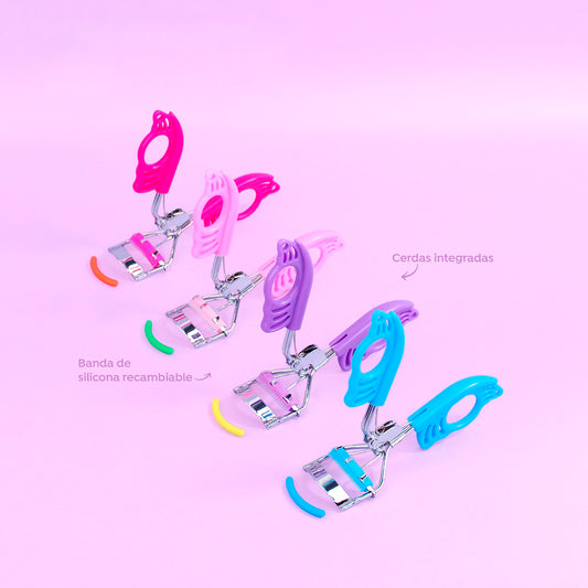 Rizador de pestañas Mariposa Curl Bellespa con mango calado diseño mariposa en colores fucsia, rosa, morado y celeste, cerdas integradas y banda de silicona recambiable sobre fondo rosa