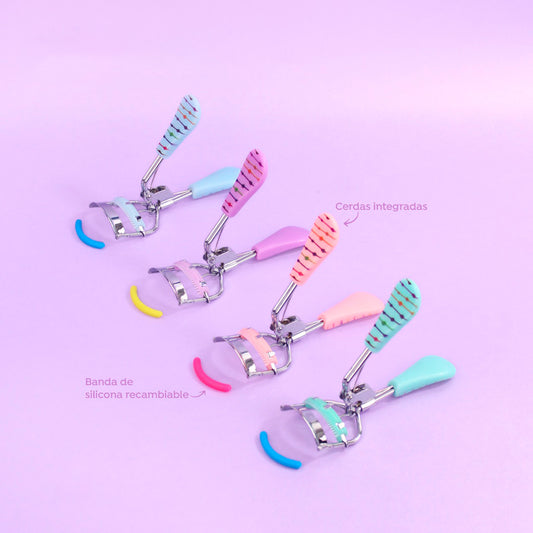 Rizador de pestañas Presión Touch Dot Print con mango bicolor estampado de puntos en colores celeste, lila, rosa coral y menta, cerdas integradas y banda de silicona recambiable sobre fondo lila