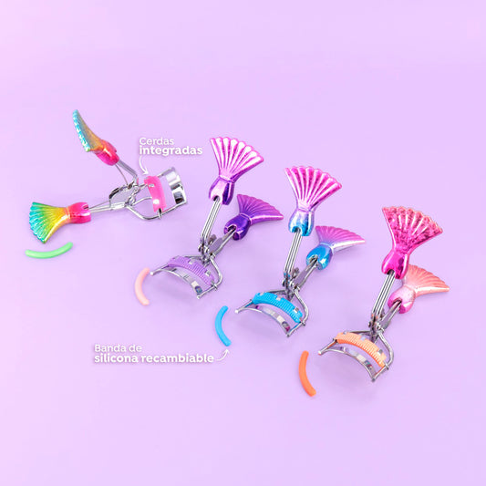 Rizador de pestañas Sirena Mermaid Curl con mango metálico tornasolado diseño cola de sirena en colores arcoíris, morado, celeste y rosa, cerdas integradas y banda de silicona recambiable sobre fondo lila