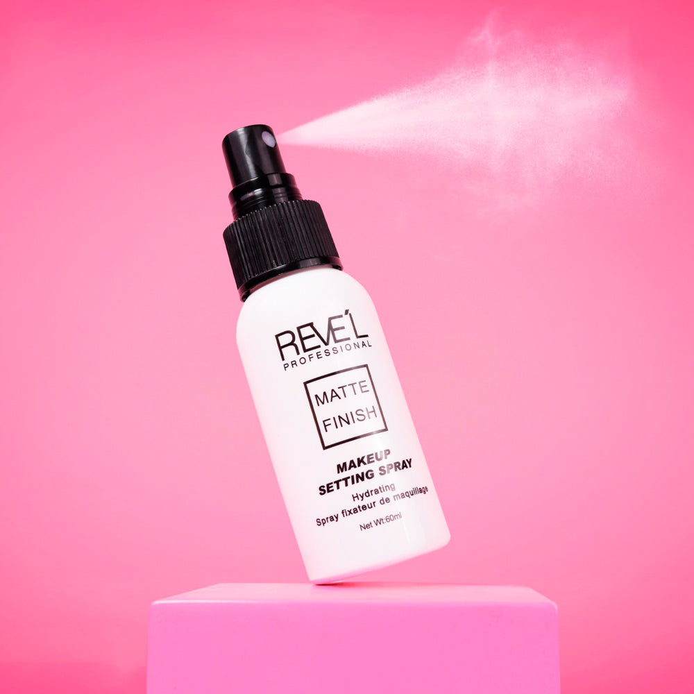 Sellador de maquillaje Matte Finish Hydrating Setting Spray Reve'l Professional en envase blanco con tapa negra sobre fondo fucsia